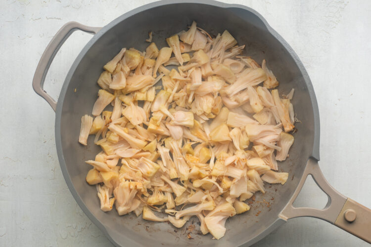 Shredded jackfruit in a large skillet with neutral oil.