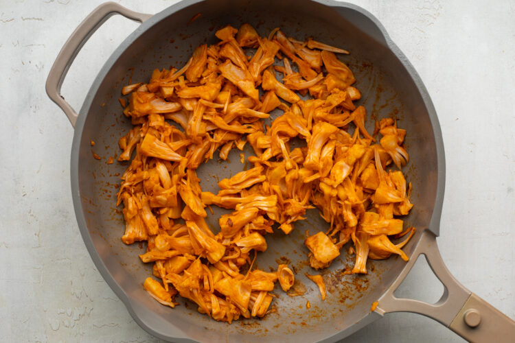 Shredded jackfruit coated in buffalo sauce and thinned with water in a large skillet.