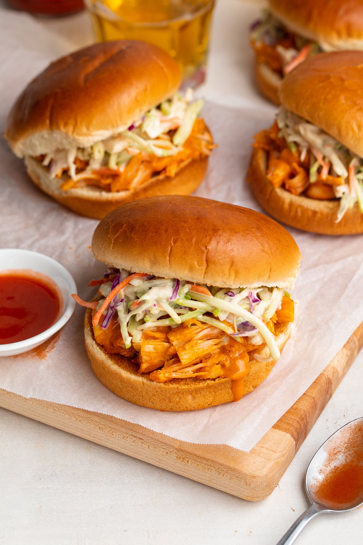 3/4-angle view of buffalo jackfruit sandwiches on a wooden cutting board covered in parchment paper.