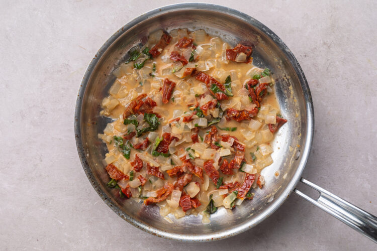 White wine reduction sauce with fresh basil and sun-dried tomatoes in a large skillet.
