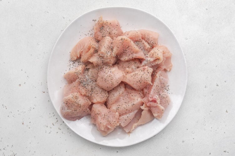 Boneless, skinless chicken breasts cut into 1-inch cubes and piled on a white plate ahead of marinating.