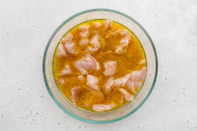 Boneless, skinless chicken breast chunks marinating in a mixture of white wine, olive oil, and lemon juice in a large glass mixing bowl.