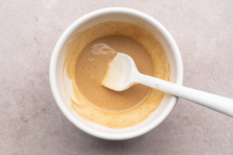 Keto honey mustard sauce in a small white mixing bowl with a white silicone spatula.
