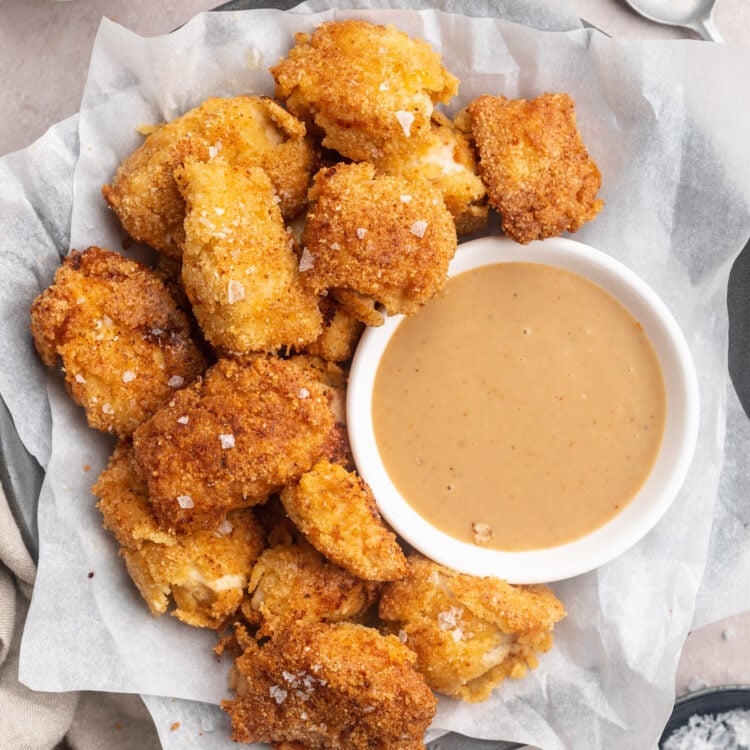 Overhead view of a plate, lined with parchment paper, holding keto chicken nuggets and a ramekin of keto honey mustard sauce.