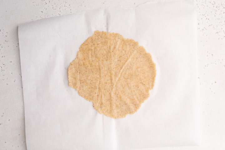 Keto taco tortilla dough rolled into a tortilla shape on a sheet of parchment paper.