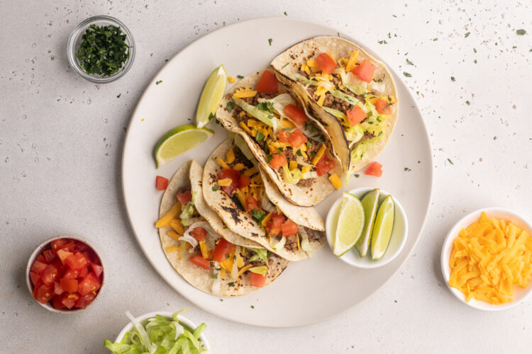Keto tacos on a plate with toppings, lime wedges, and bowls of garnish surrounding.