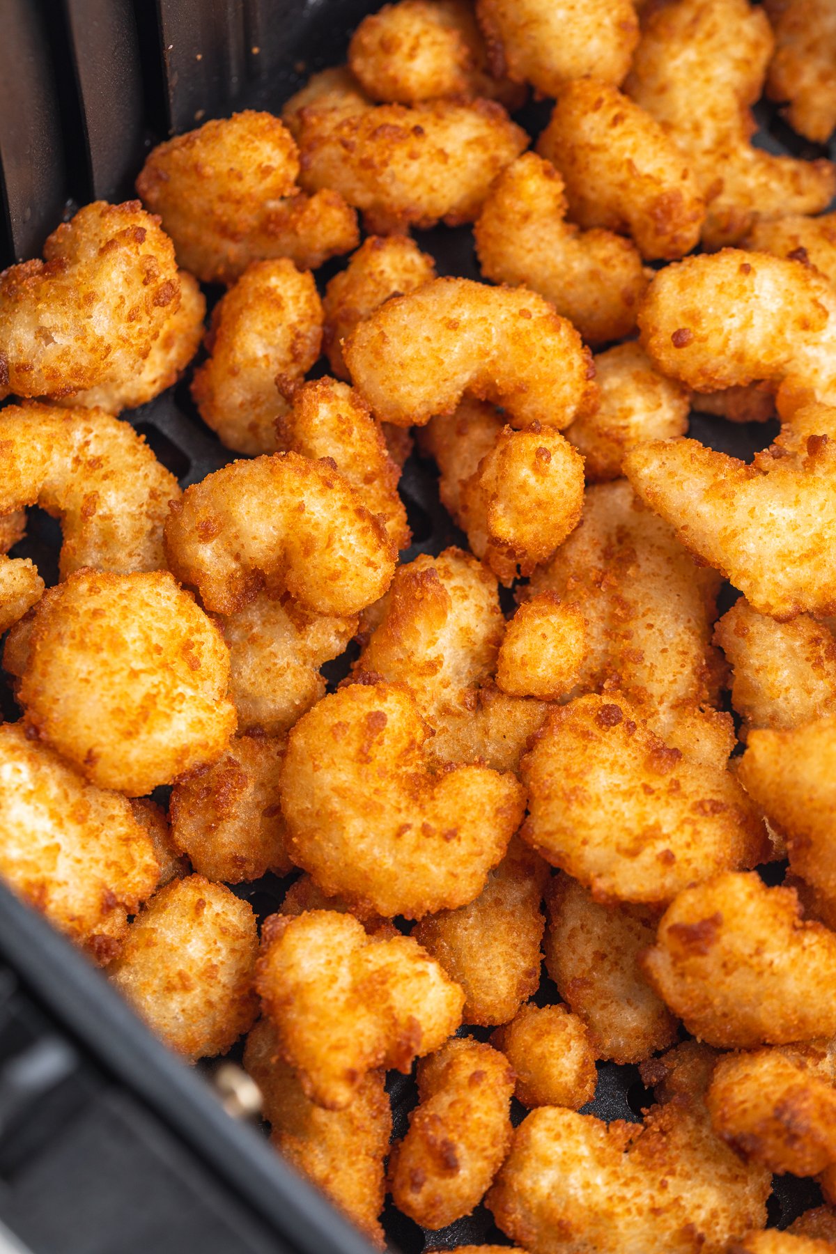 Close-up look at golden, crispy, air fried popcorn shrimp in an air fryer basket.