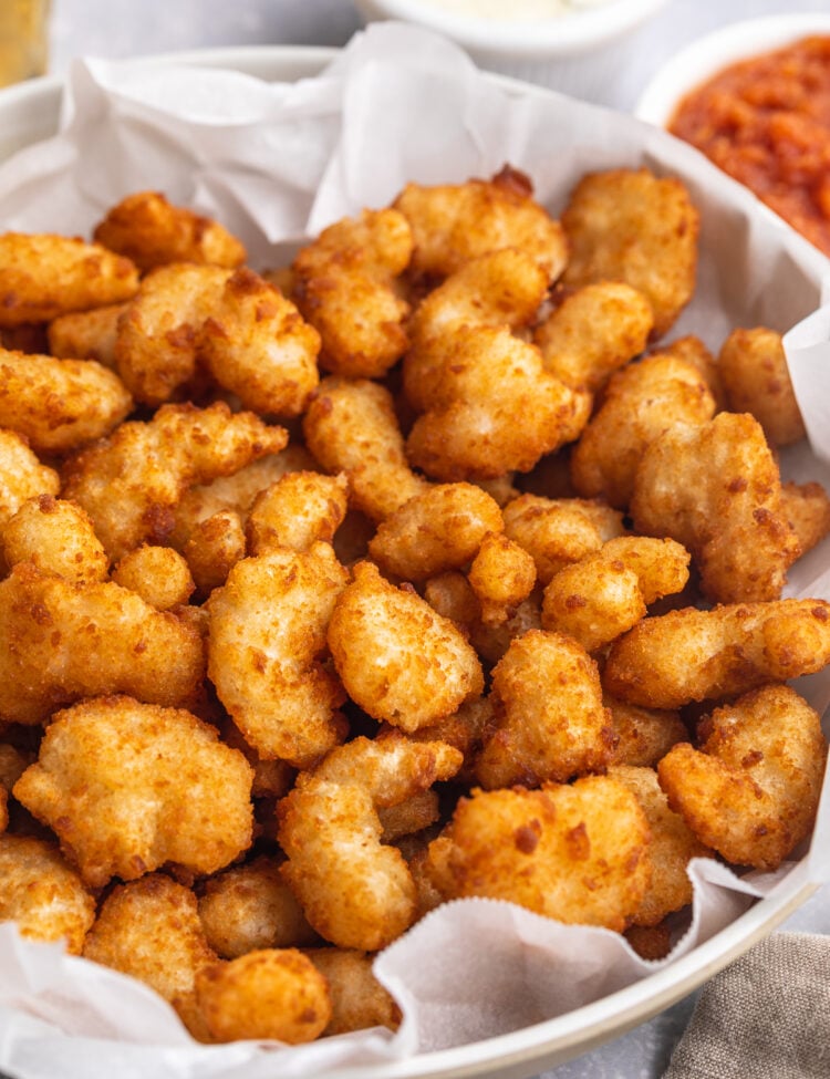 Overhead, angled photo showing a large white bowl filled with air fryer popcorn shrimp. In the background are ramekins of tartar sauce and ketchup.