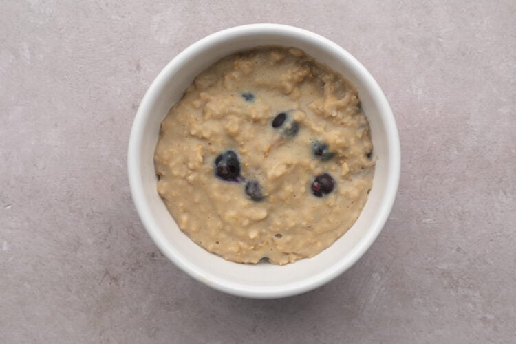 Top-down look at a white bowl filled with blueberry vanilla protein oatmeal on a neutral table.