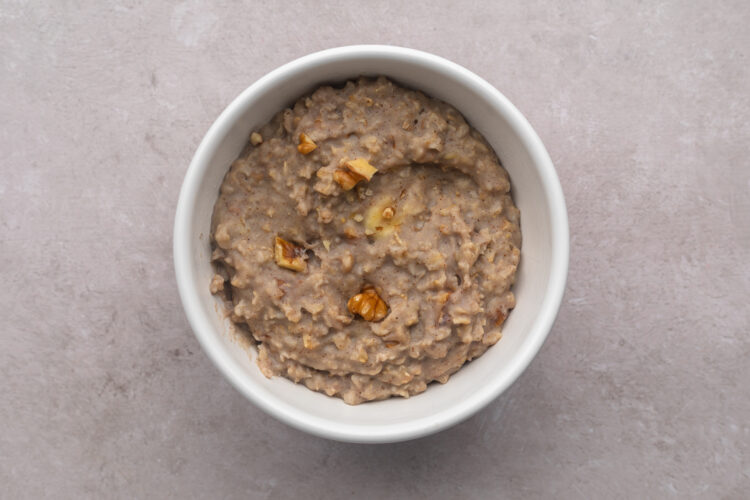 Top-down view of a white bowl filled with banana nut protein oatmeal topped with slivers of chopped walnuts.