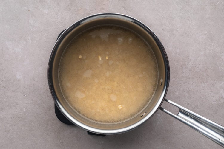 Uncooked, dry rolled oats in a silver saucepan with a single handle, with water covering the oats.