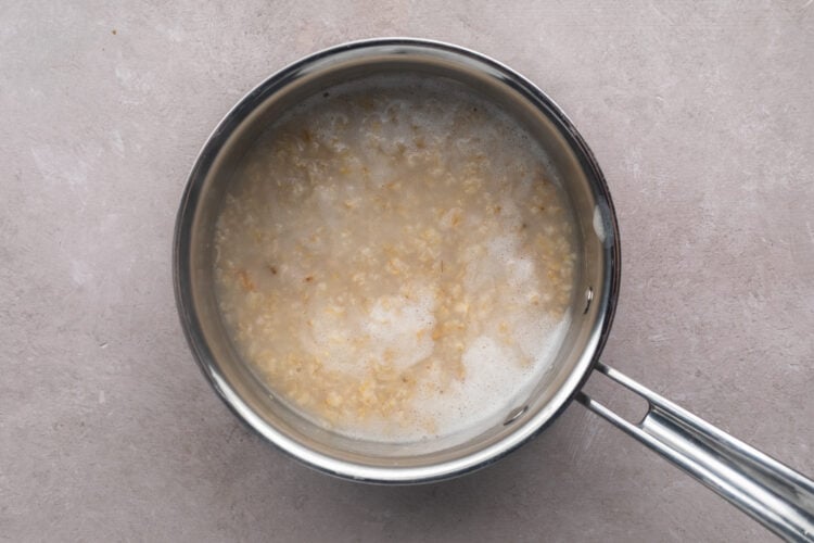 Cooked oatmeal in a silver saucepan with a single handle, showing less water than before.