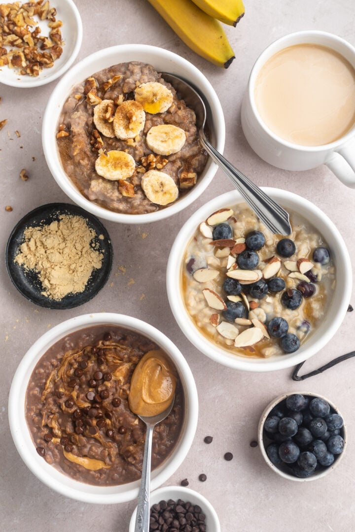 Overhead view of 3 different flavors of protein oatmeal, each in a small white ramekin on a neutral tabletop.