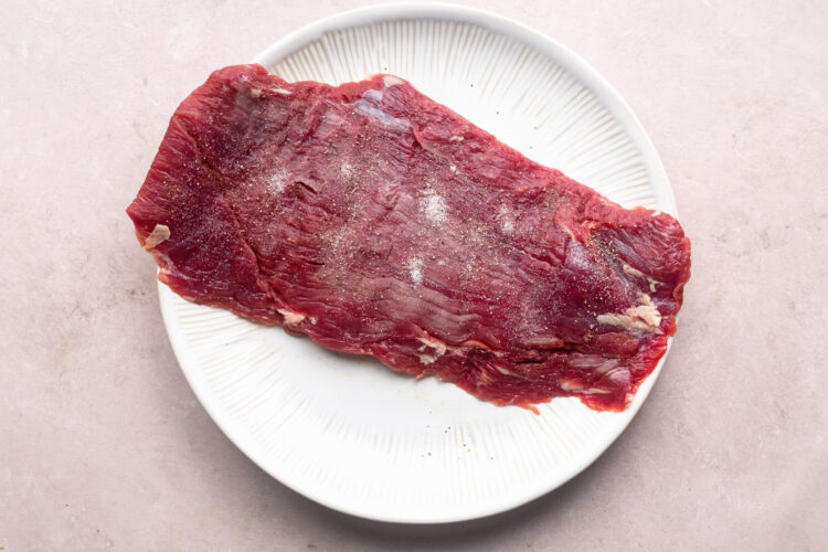 Raw flank steak on a large white plate.
