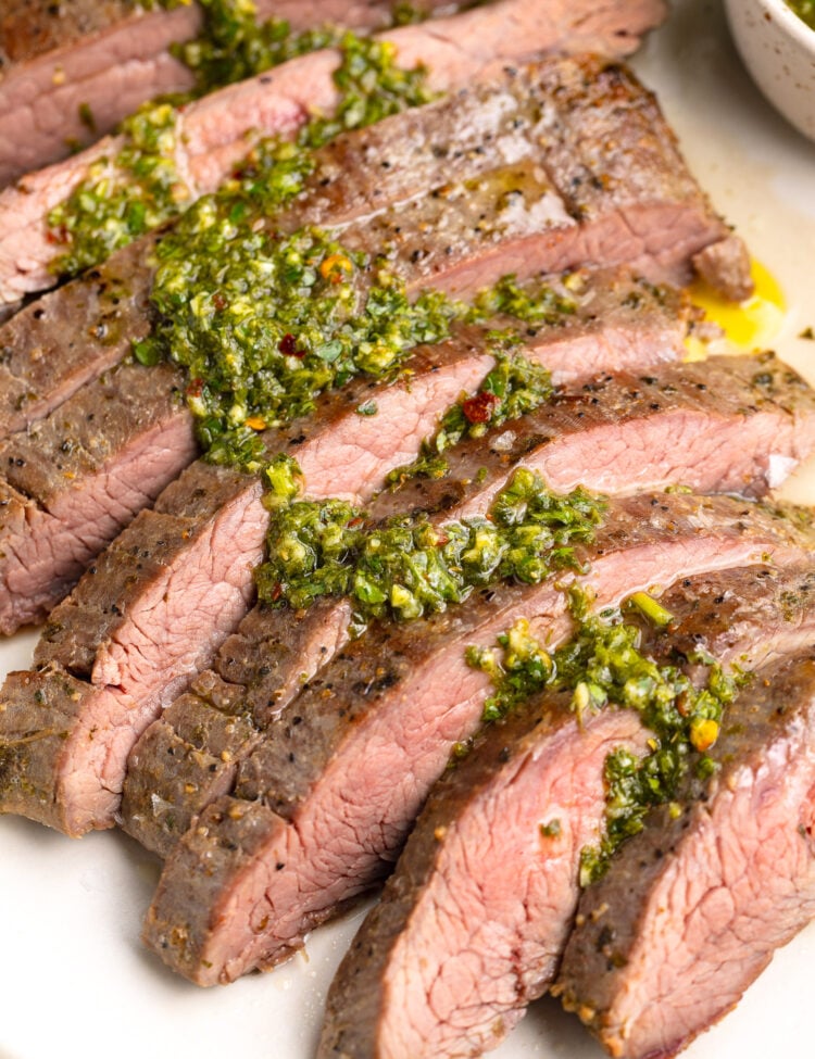 Sous vide flank steak, sliced thin and topped with green chimicuhrri resting on a platter.