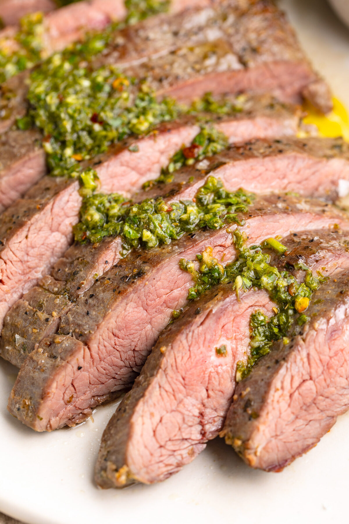 Sous vide flank steak, sliced thin and topped with green chimicuhrri resting on a platter.