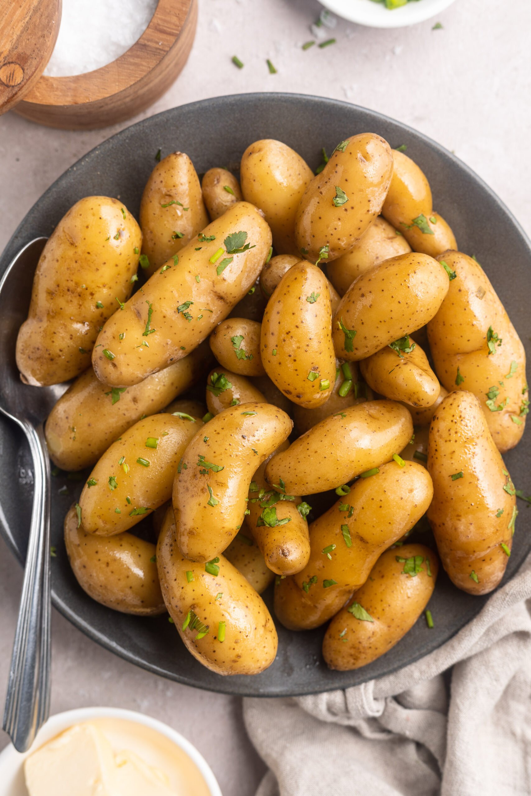 Overhead, top-down photo of sous vide fingerling potatoes in a shallow grey bowl. The brown potatoes are a little shiny and peppered with green herbs.