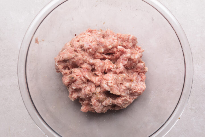 Whole30-compatible breakfast sausage mixture in a large glass mixing bowl on a white countertop.