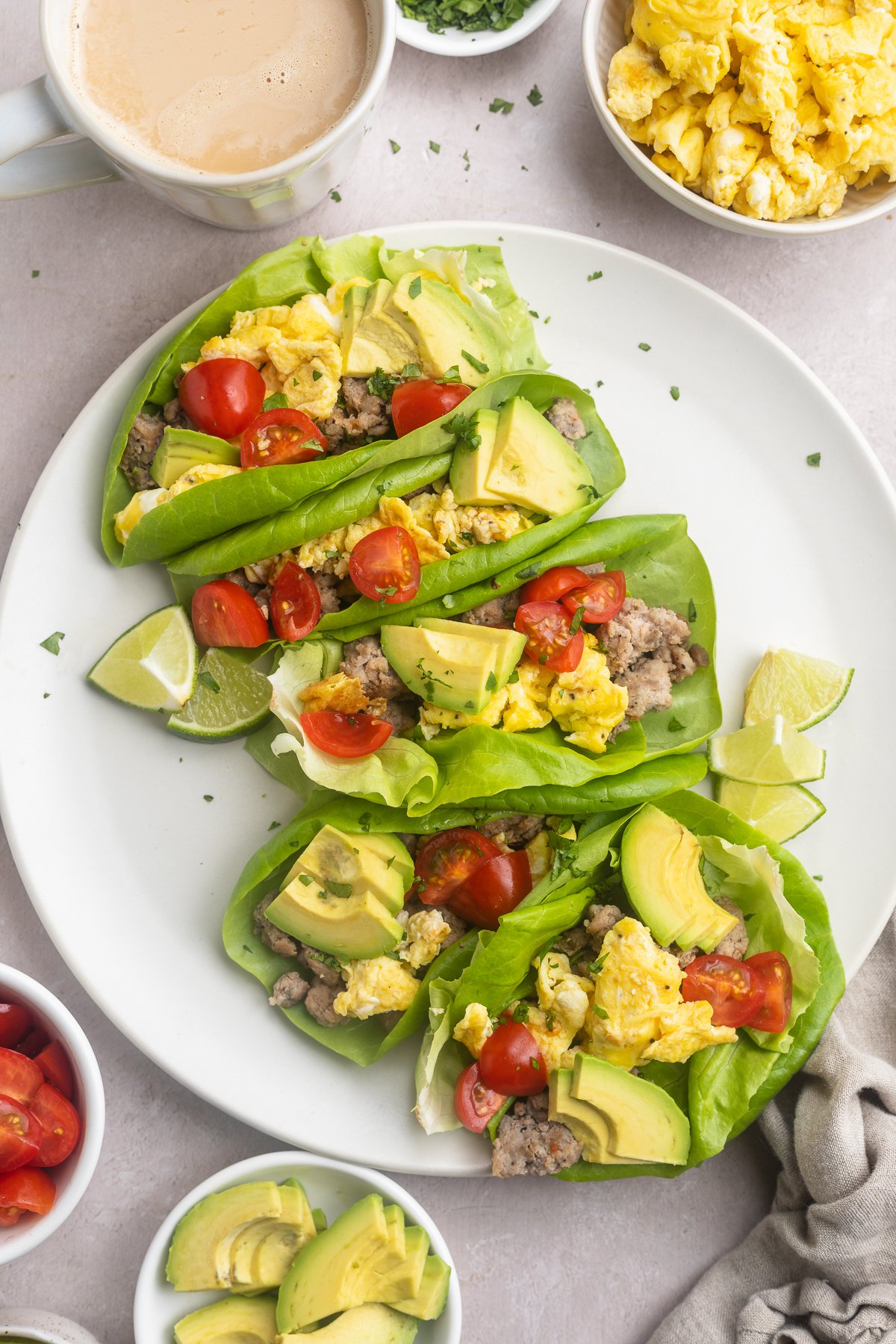 Overhead, zoomed out look at Whole30 breakfast tacos on a round white plate with bowls of ingredients surrounding.