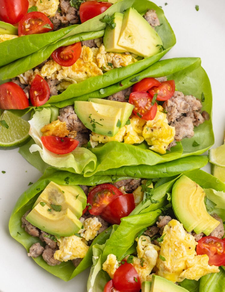 5 Whole30 breakfast tacos filled with scrambled eggs, slices of avocados, halved cherry tomatoes, and breakfast sausage.