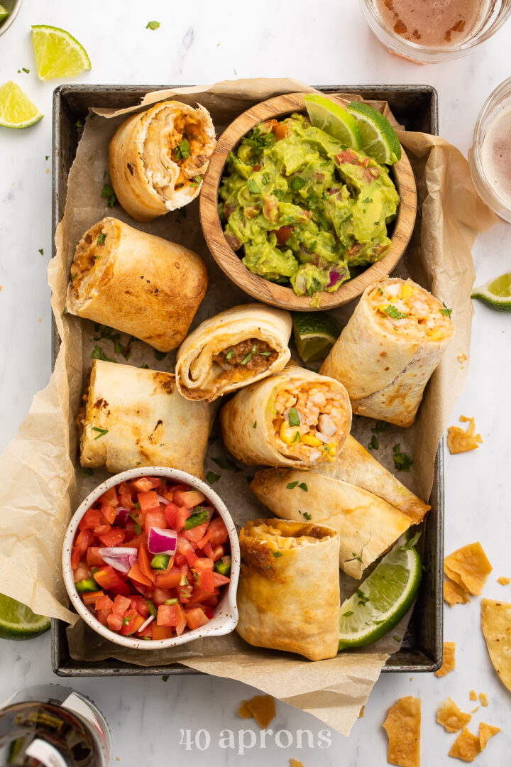 Top-down view of frozen burritos cooked in the area fryer, halved and arranged in a baking pan with guacamole and fresh salsa.