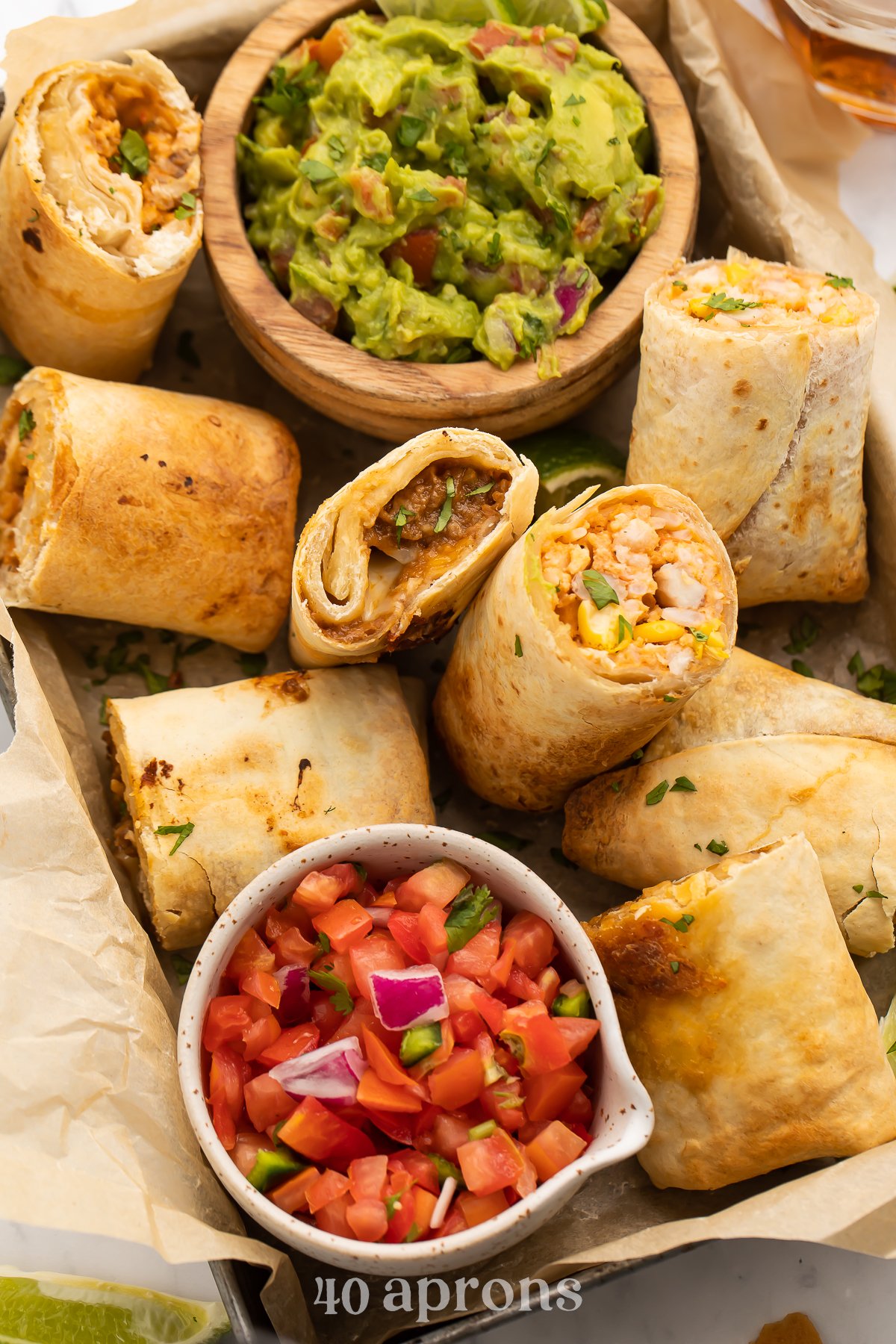 Top-down look at a dark silver baking pan, angled from top left corner to bottom right corner, holding air fryer frozen burritos with guac and pico de gallo.
