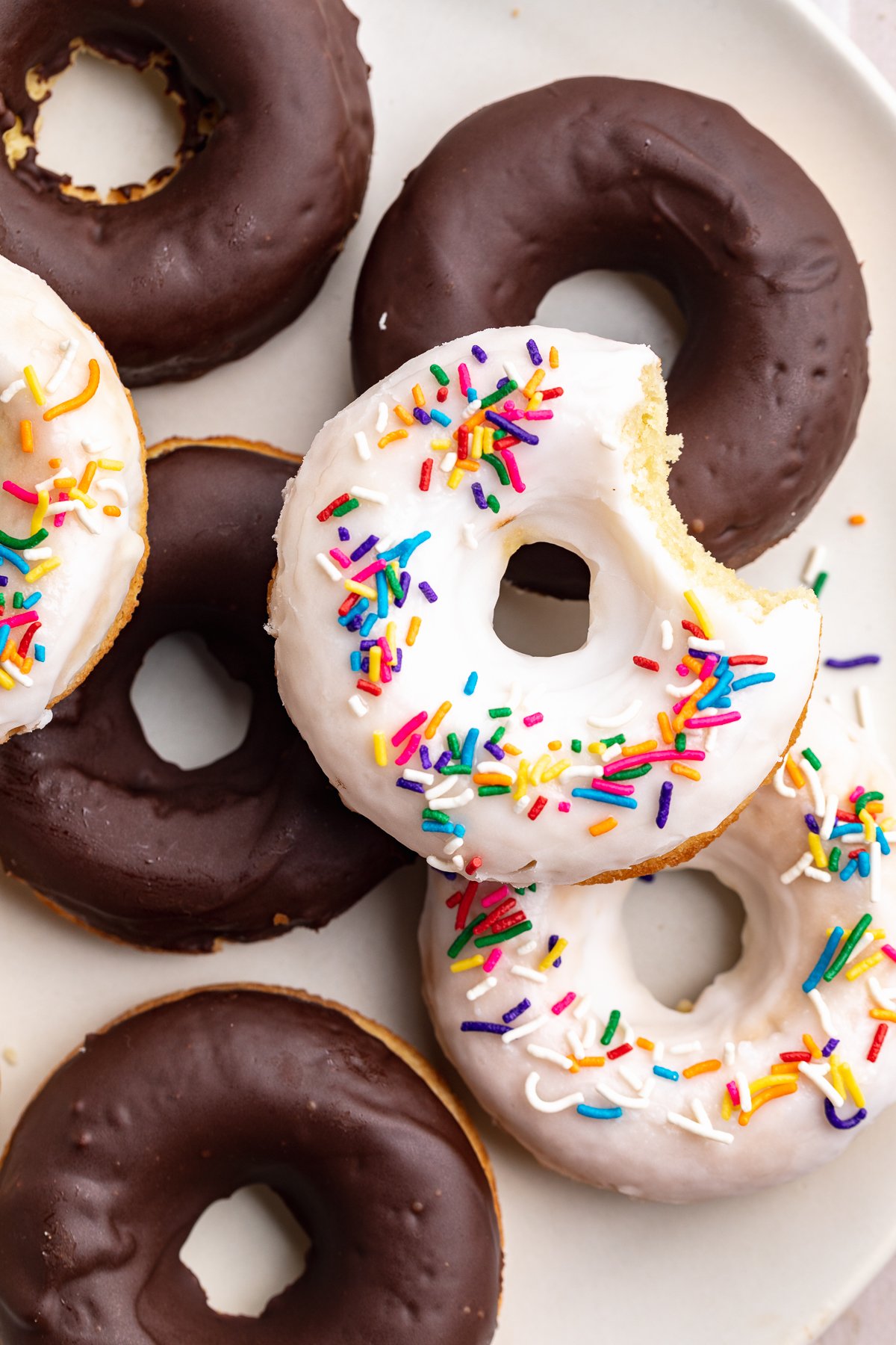 Overhead look at chocolate and vanilla glazed donuts piled up on a plate.