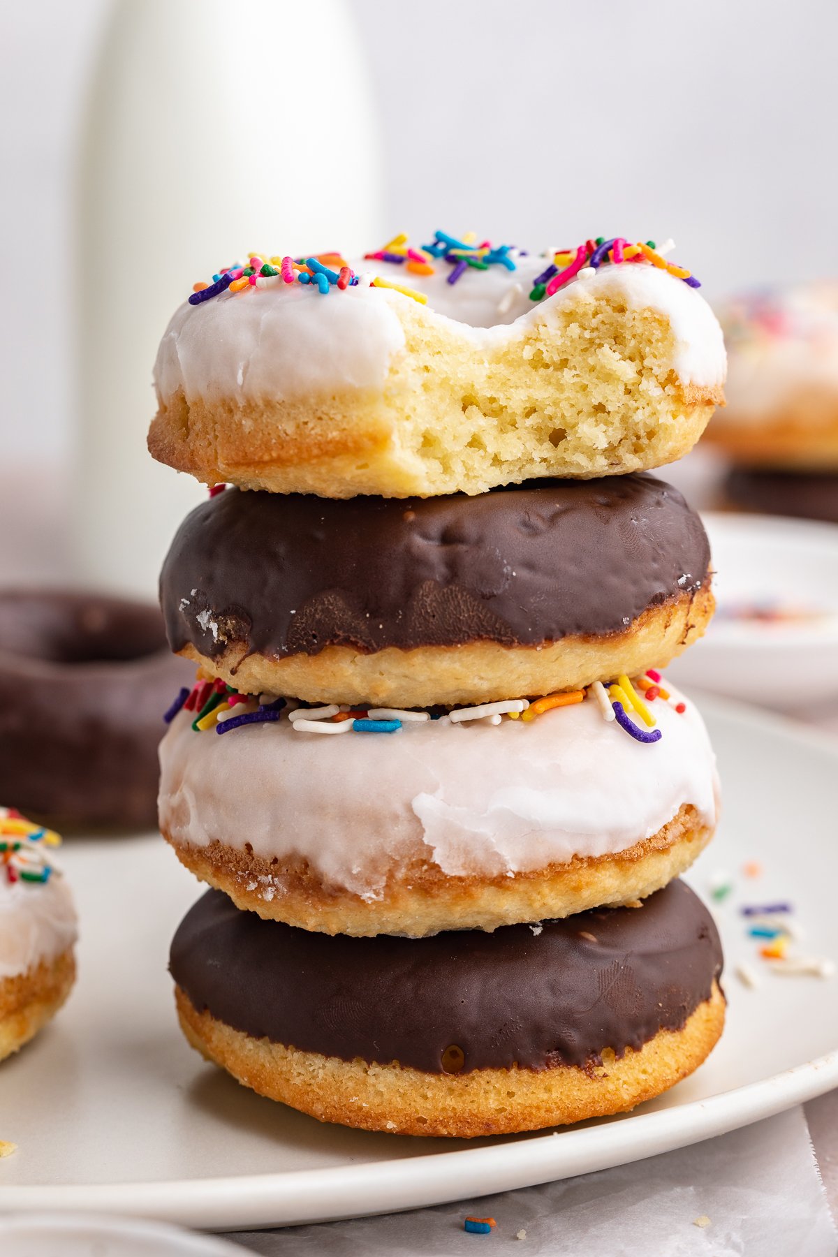 4 keto donuts, 2 vanilla and 2 chocolate glazed, stacked on top of each other with one bite missing from the top donut.