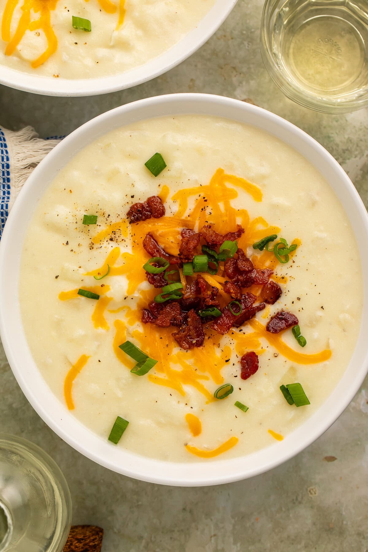 Creamy old-fashioned potato soup in a white bowl topped with shredded cheddar cheese, bacon, and green onions.