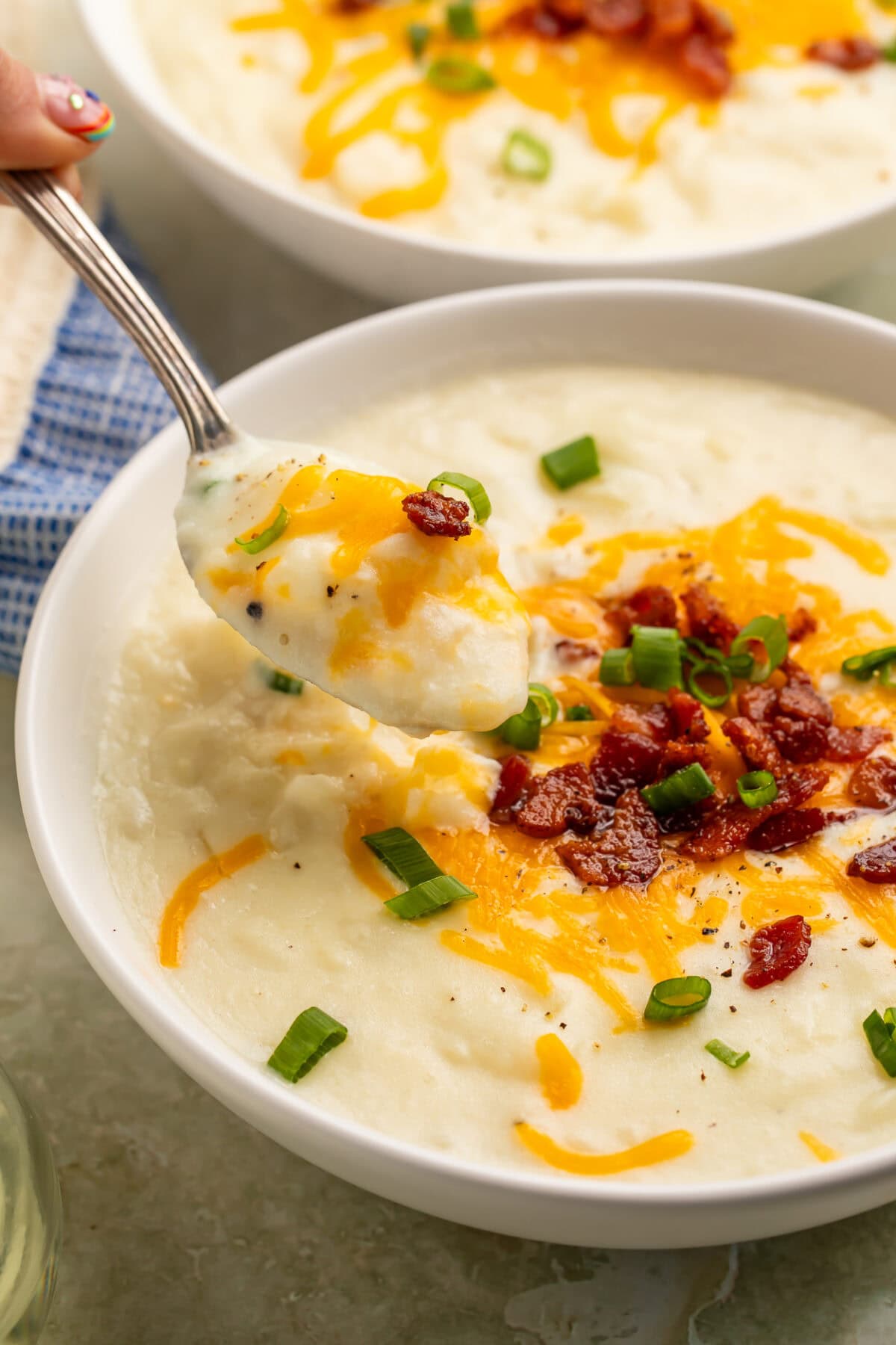Two white bowls of creamy potato soup garnished with cheese and bacon on a table with water glasses.