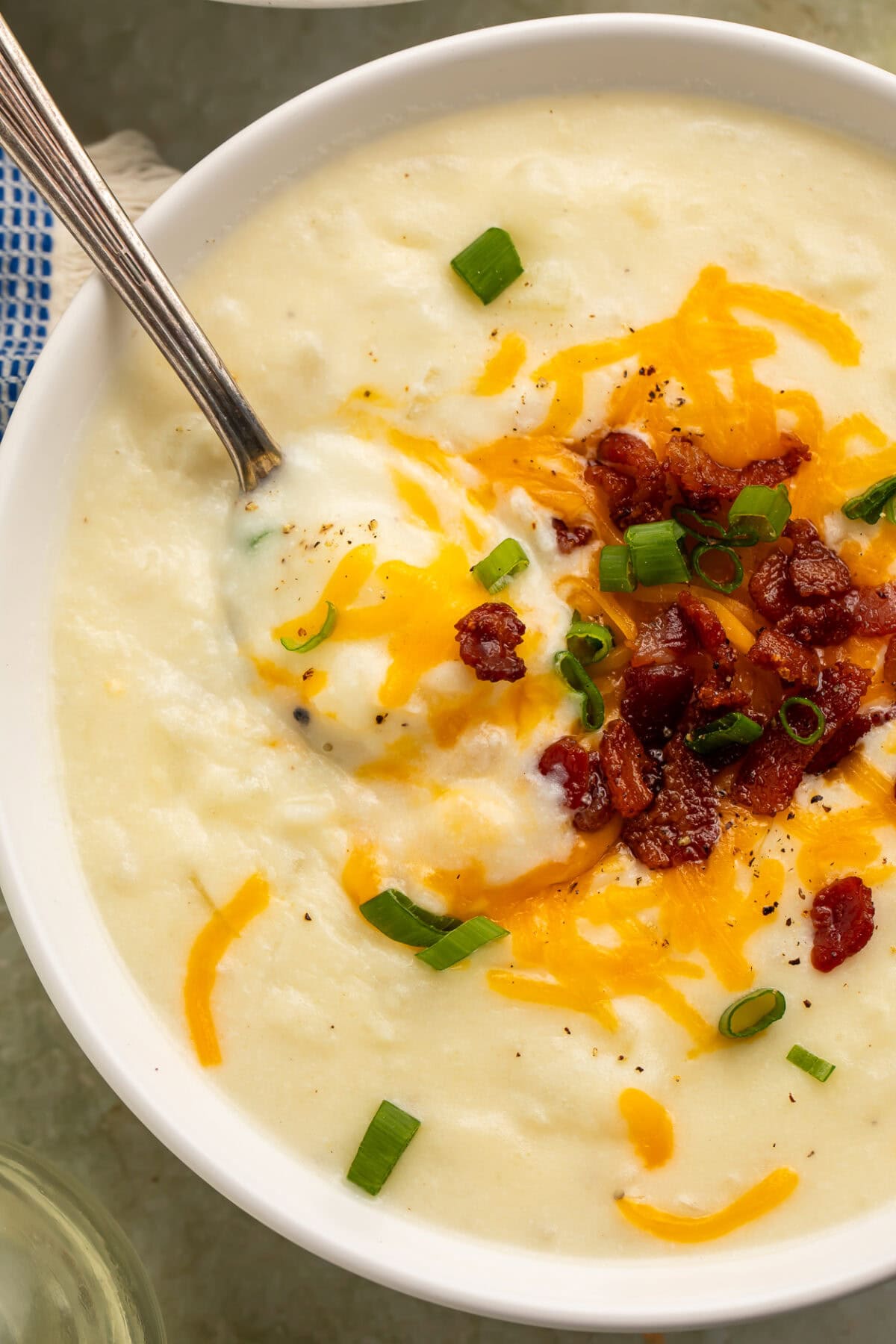 Close-up overhead view of creamy potato soup in a white bowl with melted cheese, bacon, and green onions.