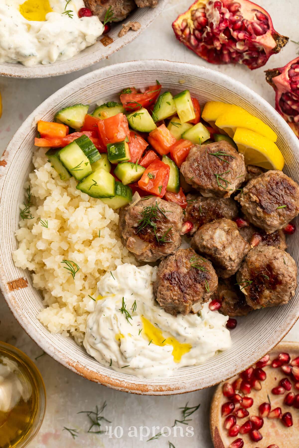 Whole30 gyro meatballs in a large bowl with tabbouleh, cucumber salsa, cauliflower rice, and Whole30 tzatziki.