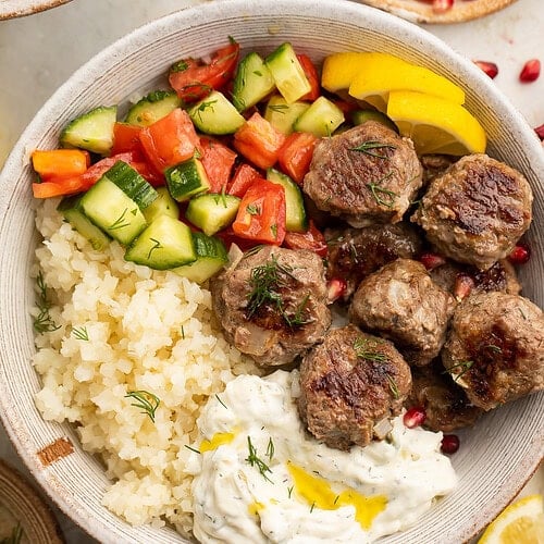 Whole30 gyro meatballs in a large bowl with tabbouleh, cucumber salsa, cauliflower rice, and Whole30 tzatziki.