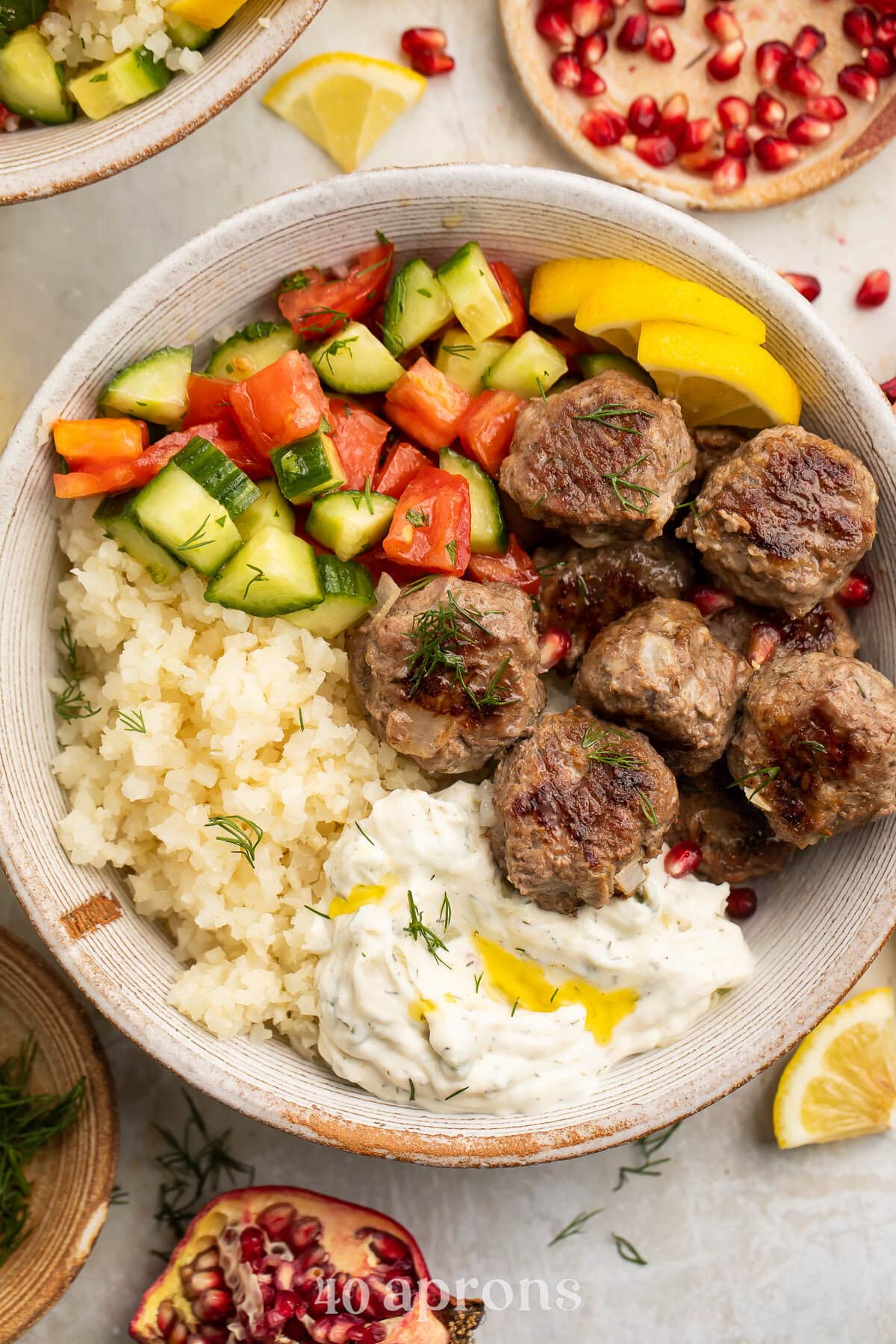 Whole30 gyro meatballs in a large bowl with tabbouleh, cucumber salsa, cauliflower rice, and Whole30 tzatziki.