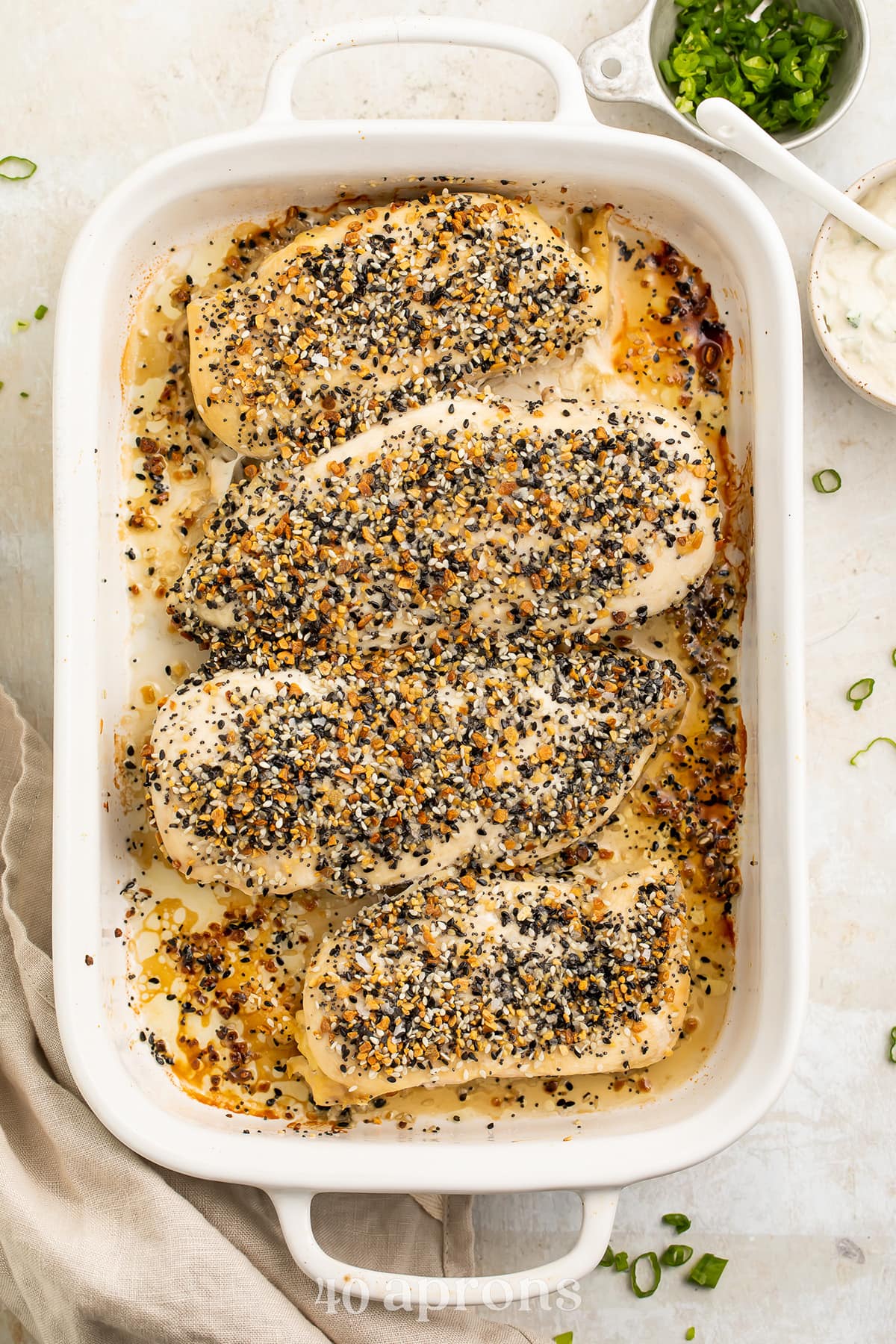 4 Whole30 Everything Bagel chicken breasts in a white rectangular casserole dish on a neutral table.
