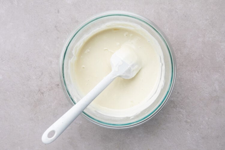 Melted white chocolate and coconut oil in a large glass mixing bowl with a white silicone spatula.