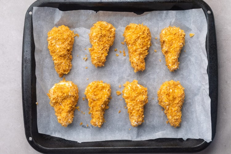 Vanilla ice cream chicken drumsticks coated in a cornflake "breading" and lined up on a baking sheet covered with parchment paper.