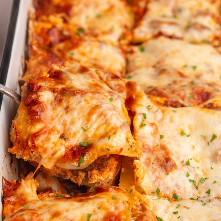 A square of gluten-free lasagna being lifted out of a casserole dish of lasagna.