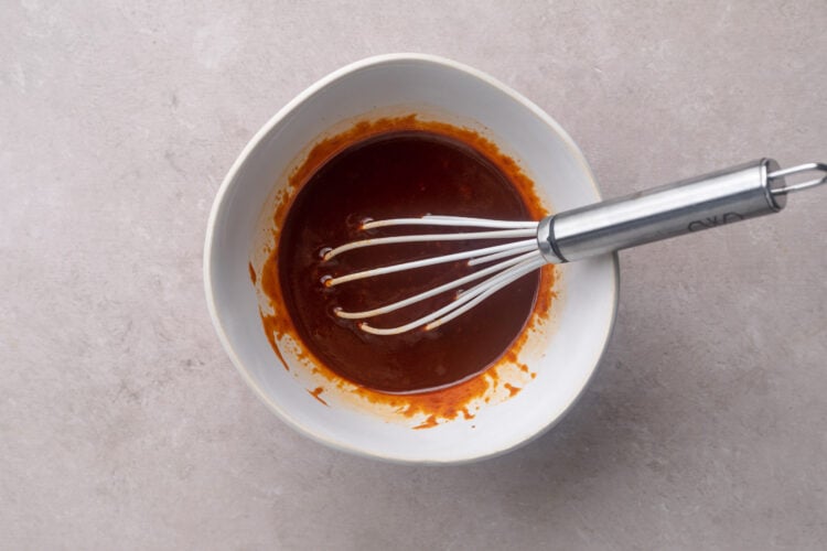 Deep red gochujang sauce in a mixing bowl with a metal whisk.