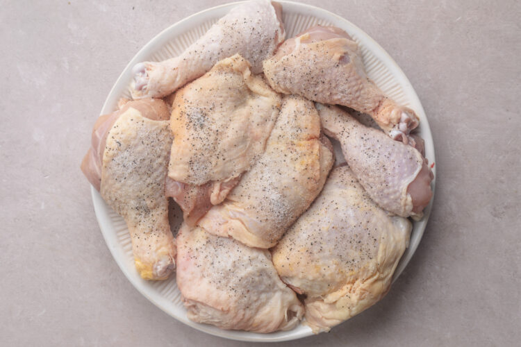 Seasoned, uncooked chicken thighs on a round white plate.
