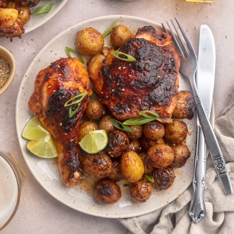 Zoomed-out view of plated gochujang chicken and potatoes with lime wedges on a round white plate.