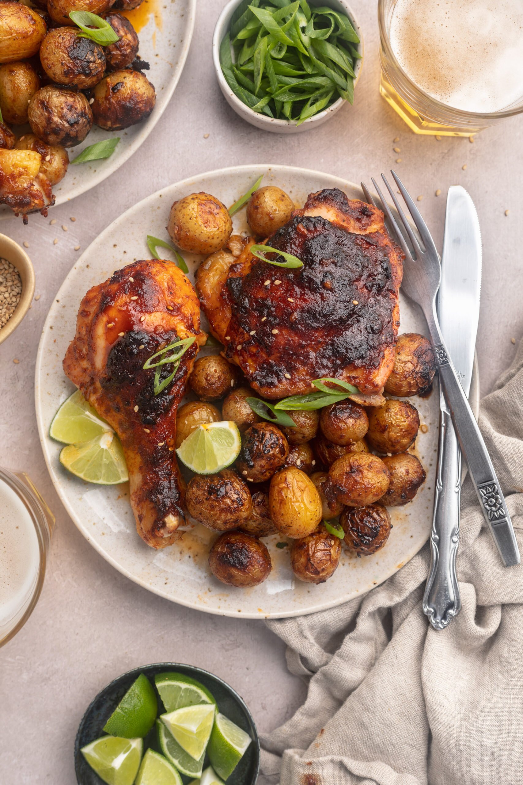 Zoomed-out view of plated gochujang chicken and potatoes with lime wedges on a round white plate.