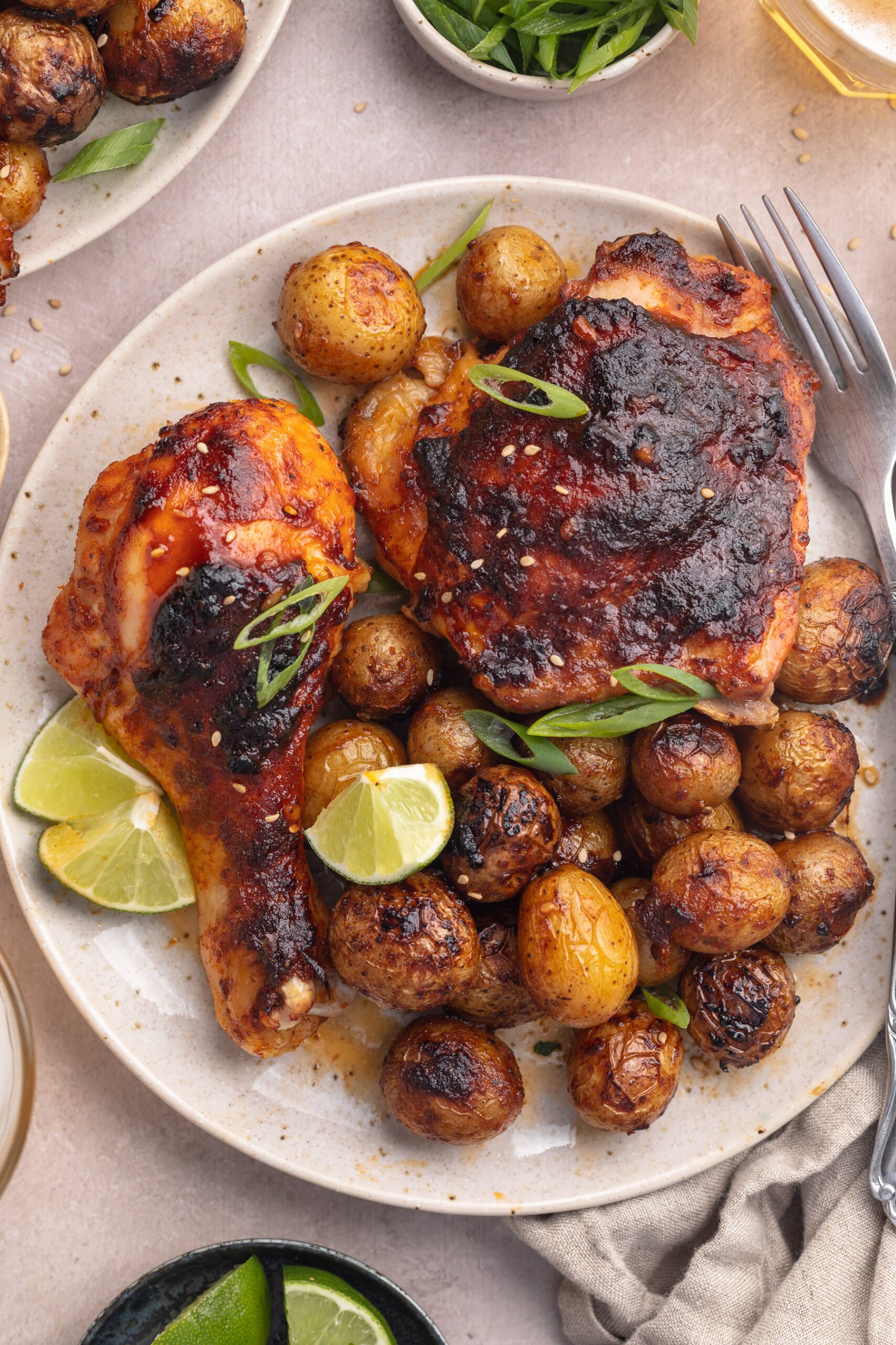 Plated gochujang chicken and potatoes with lime wedges on a round white plate.