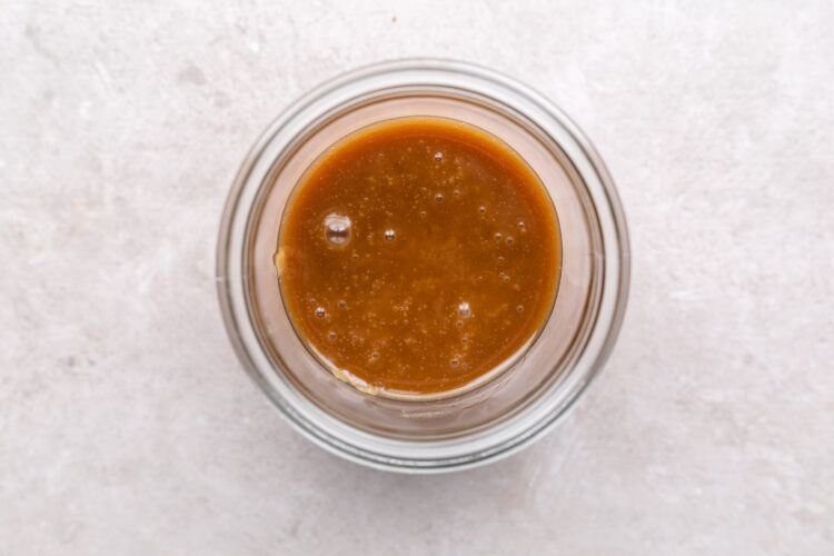 Keto caramel sauce in a glass jar on a neutral countertop.