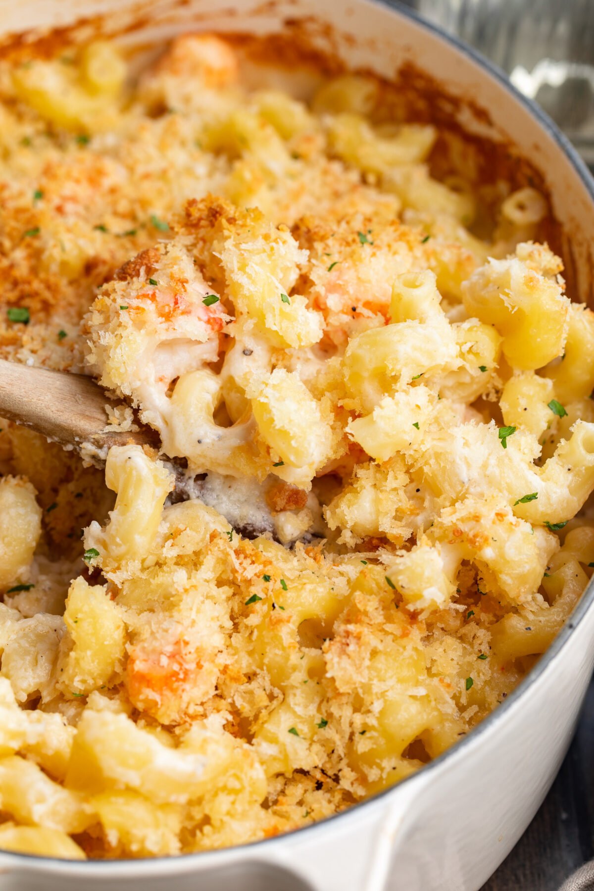 Close-up view of a scoop of lobster mac and cheese resting on a wooden spoon being lifted out of a casserole dish.