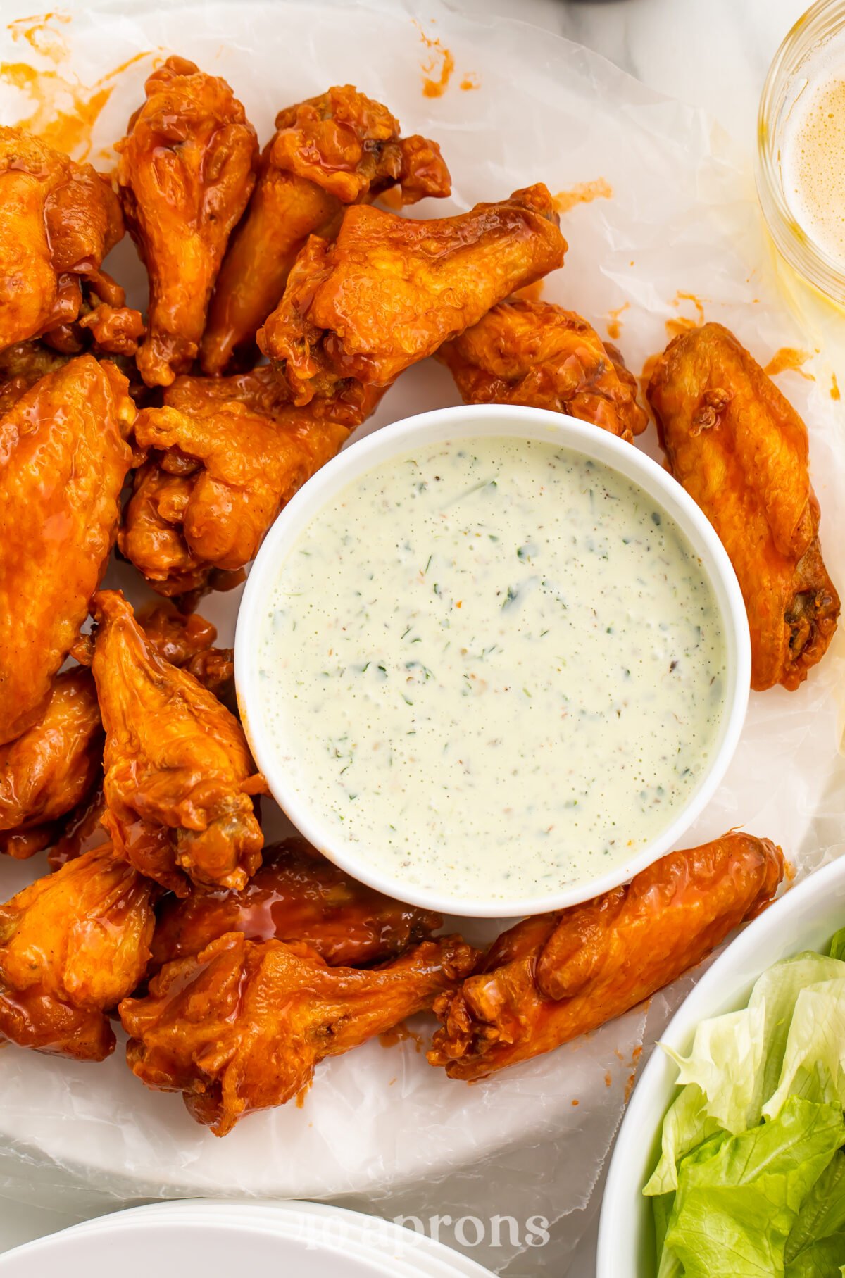 Top-down view of a bowl of chimichurri ranch dressing on a plate with bright orange buffalo chicken wings.