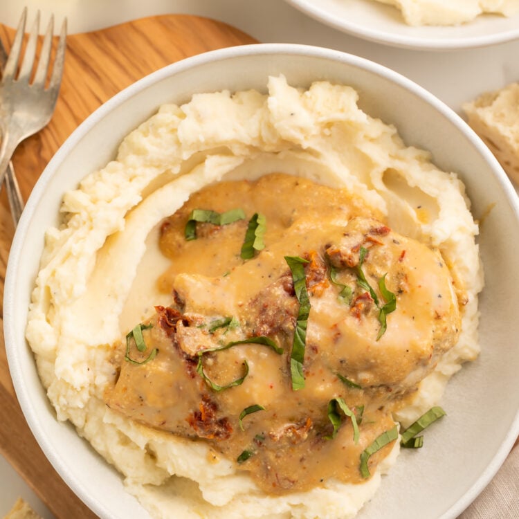 Top-down, overhead view of a Crockpot-cooked marry me chicken breast with sauce atop a bed of mashed potatoes in a large white bowl.