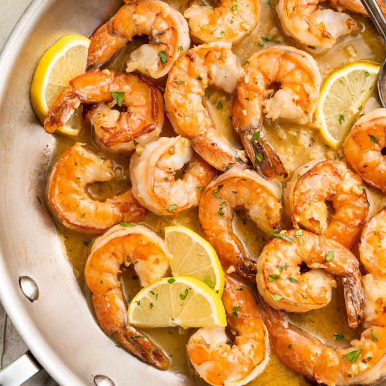 Sautéed garlic butter shrimp in a large silver skillet with lemon and parsley.