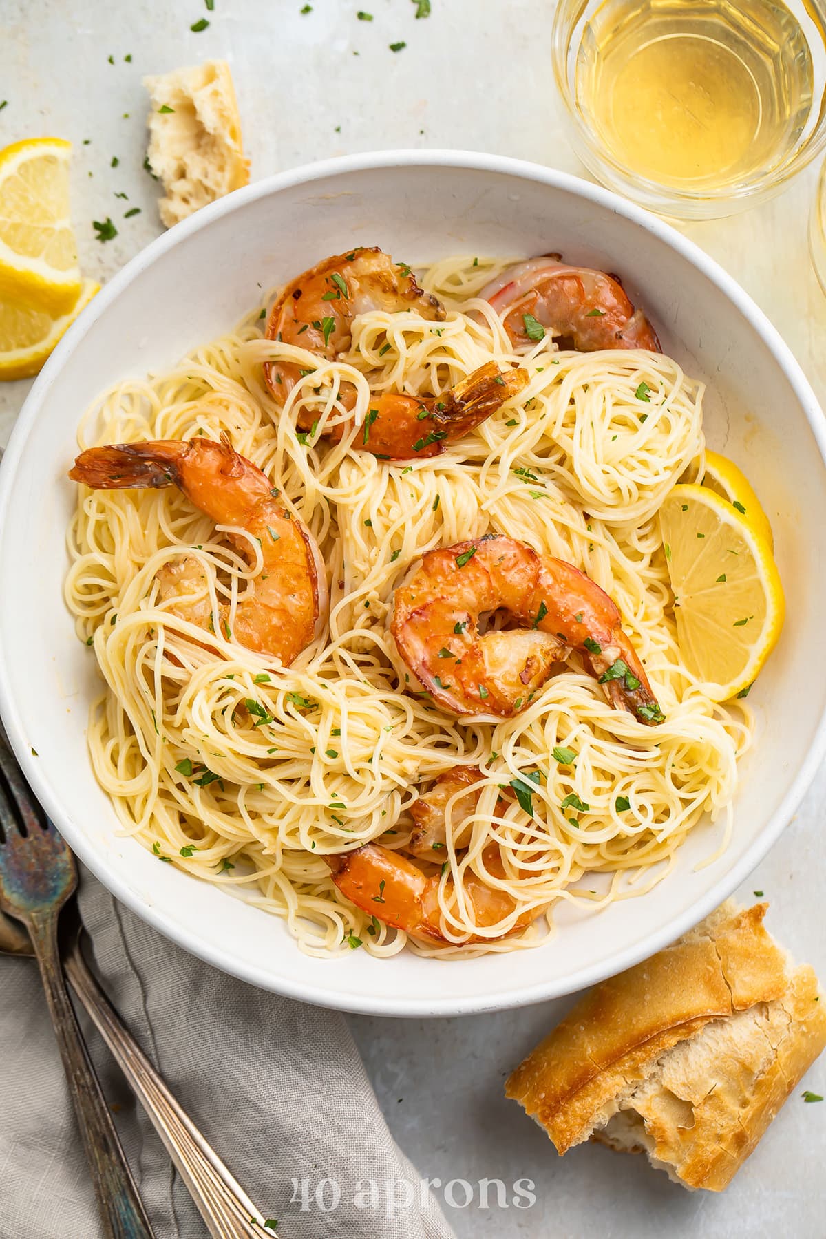 Sautéed garlic butter shrimp plated atop a bowl of angel hair pasta and garnished with parsley and lemon wedges.