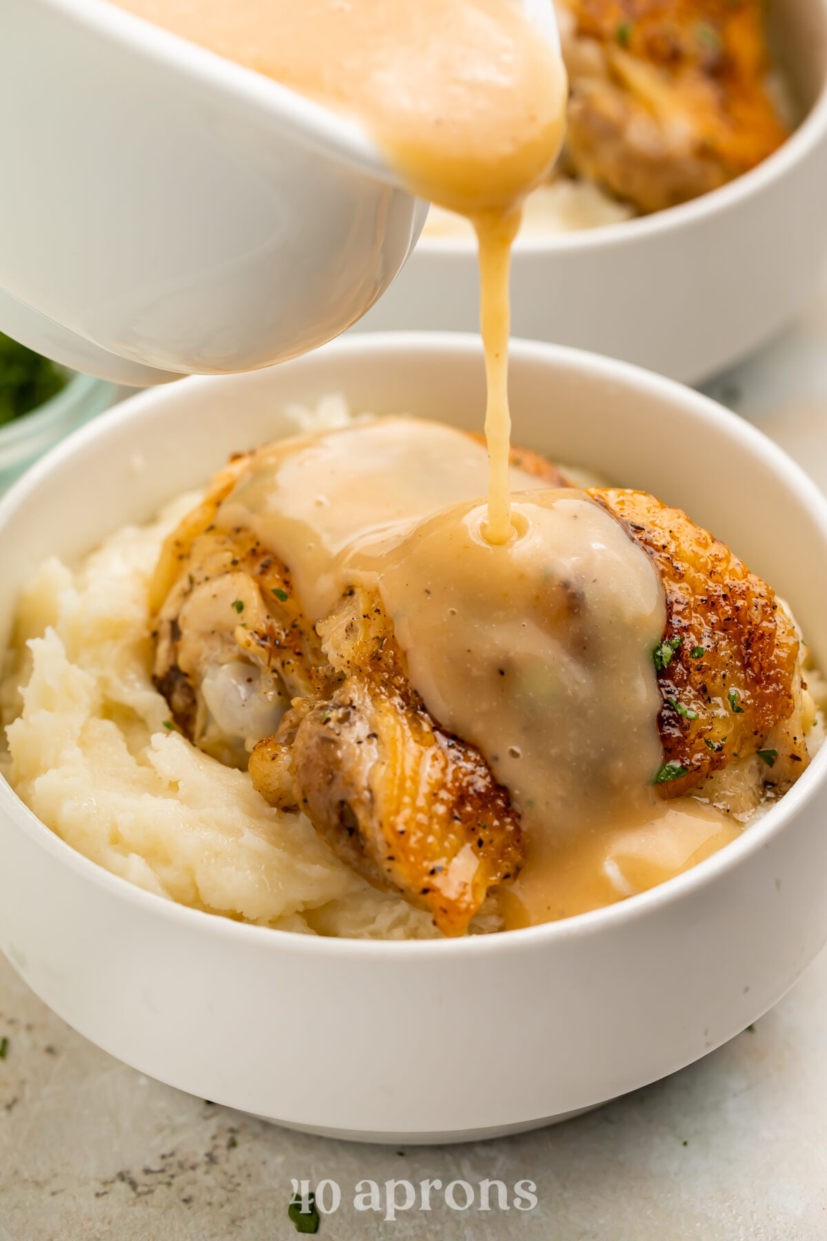 Gravy being poured over a perfectly cooked Instant Pot chicken thigh atop a bed of mashed potatoes in a bowl.